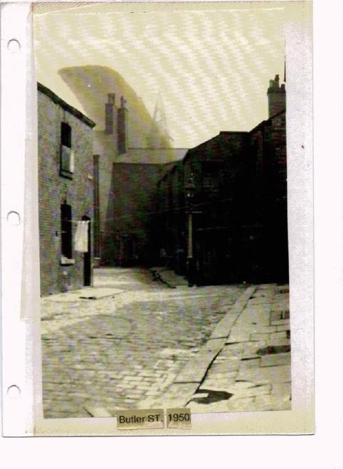A scan of a yellowed photograph of the view along Butler Street, with visible signs of age. There is a washing line hung across the street, and the top of a pointed tower barely visible in the distance. At the bottom of the photo, some text reads Butler ST. 1950.