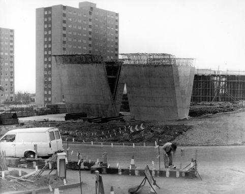 A black and white photo showing construction work on a flyover, with two large concrete structures in the centre of the frame. Behind the structures are Crossbank House and Summervale House, to the left of the frame.