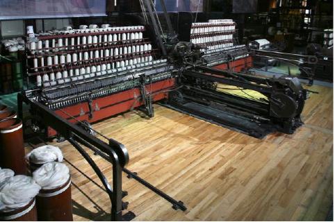 An image of cotton processing machinery on display in a museum. The machinery has lots of skeins of cotton arranged in rows, and many moving parts.
