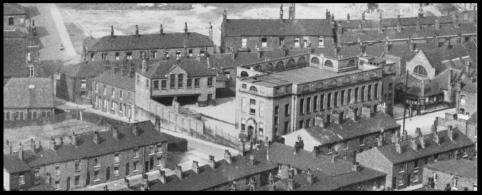 A black and white aerial photo of streets of houses, with a school at the centre of the frame.