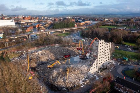 An aerial photo of the site during demolition. The road and surrounding landscape is clearly visible behind the site, as less than a quarter of one of the towers is all that remains standing.