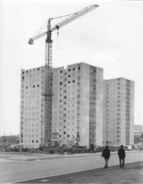 A black and white photo of Crossbank House and Summervale House during construction. There is a crane in front of the towers. There are two people walking in the foreground of the image.